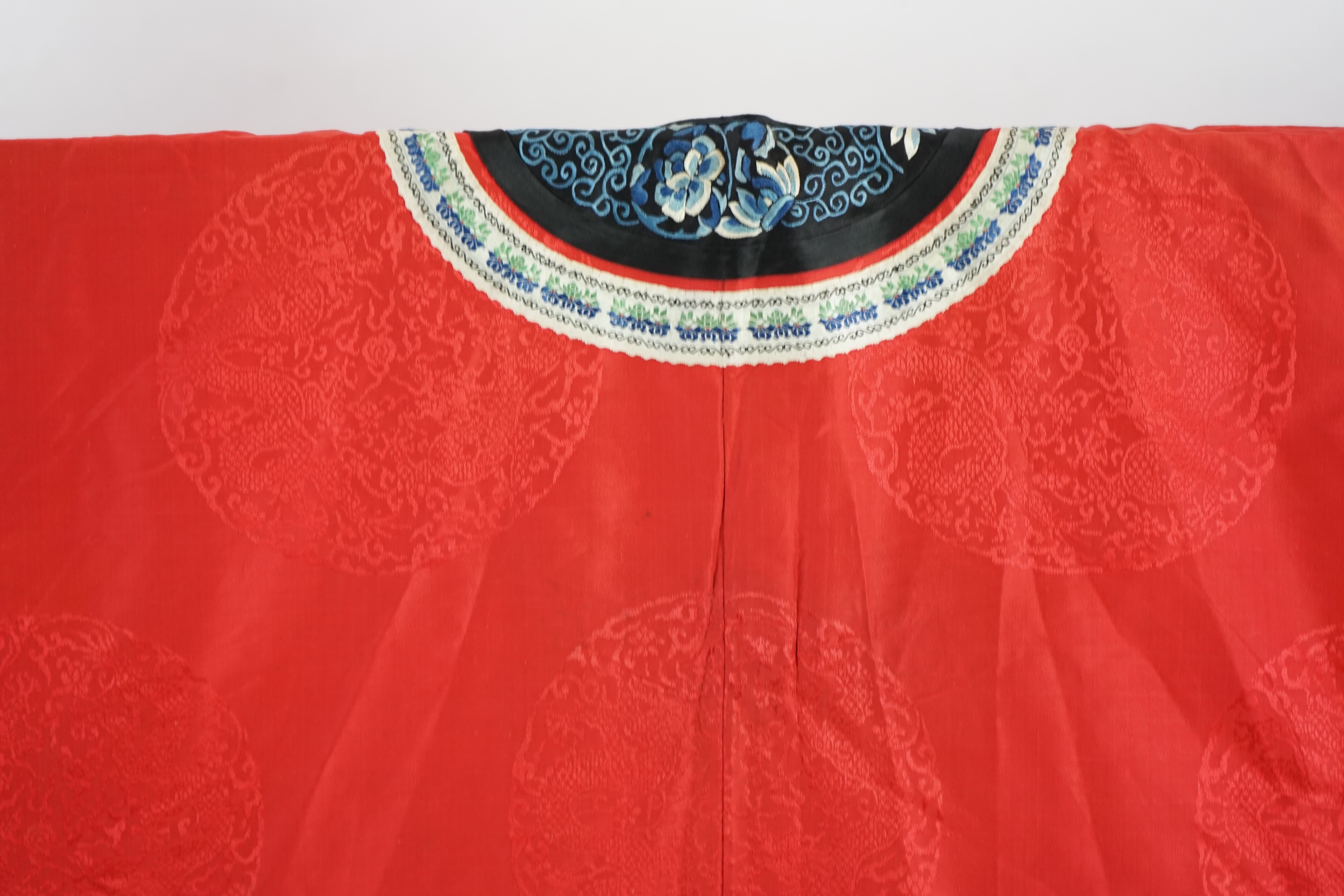 A late 19th century Chinese Manchu ladies red silk damask robe, with black and blue silk embroidered borders, ornately edged cream floral silk braiding, length from neck (back) to bottom edge 132cm long. Condition - stai